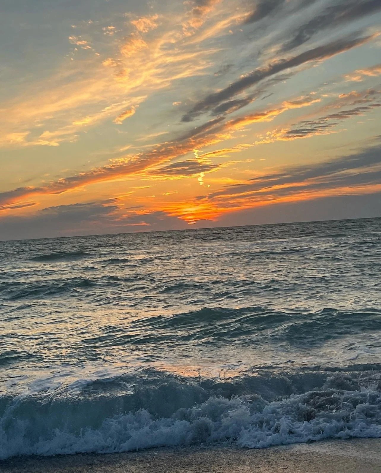 Ocean waves with an orange sunset and cloudy sky.