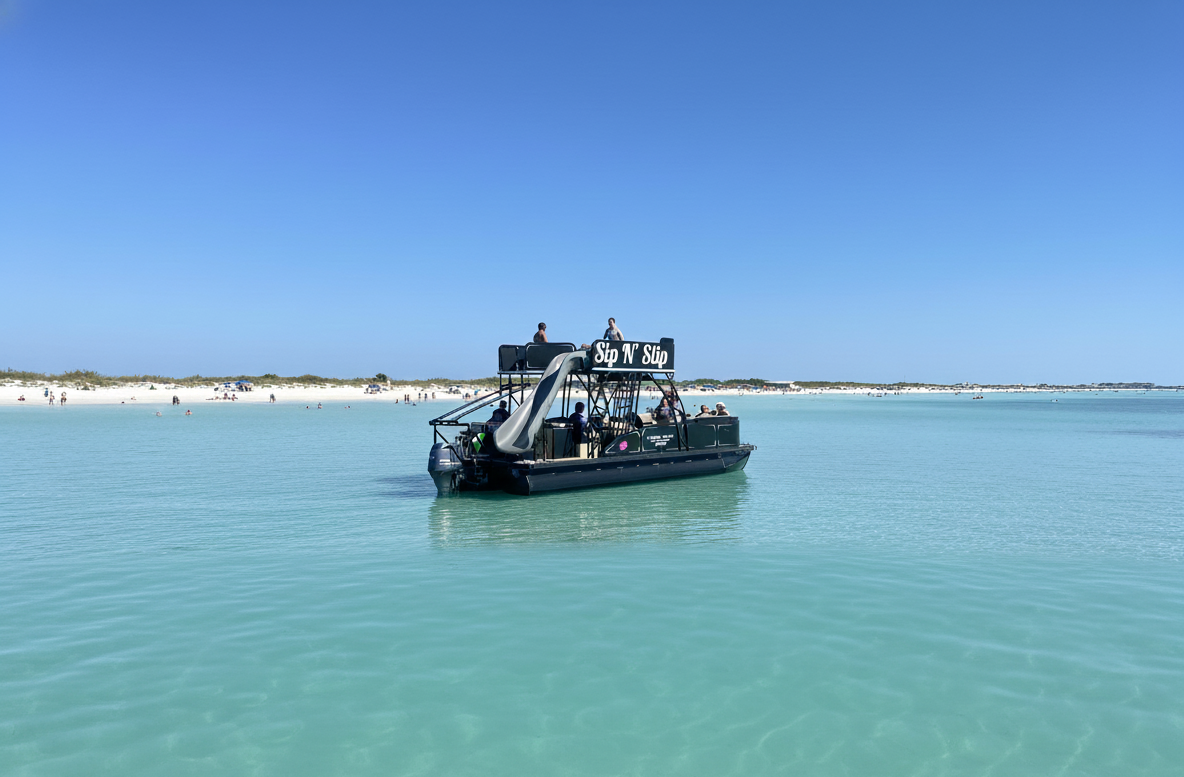 Floating bar with water slide on calm turquoise sea against a sunny beach backdrop.