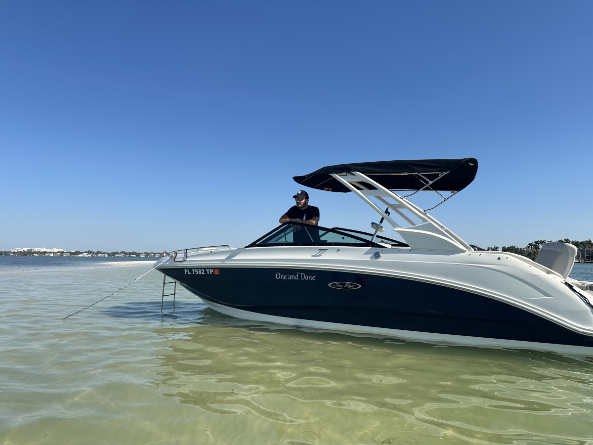 Person in a boat on calm water under a clear blue sky, with distant shoreline visible.