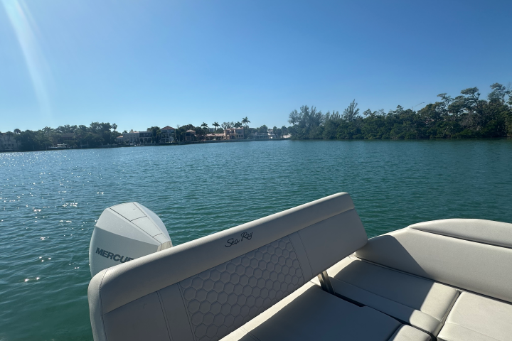 Boat with a Mercury engine on a lake with distant trees under a clear blue sky.
