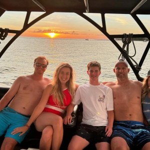 Five people posing on a boat at sunset with the ocean in the background.